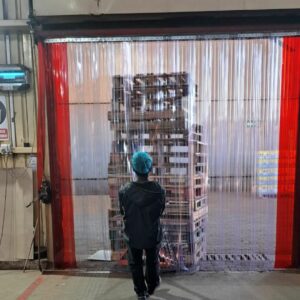 Man pulling crates in a warehouse through clear strip curtain.